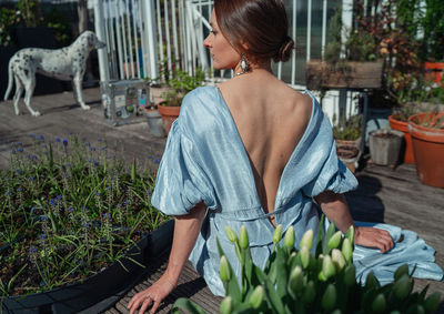 Rear view of woman sitting by potted plants outdoors