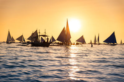 Sailboats sailing in sea against sky during sunset