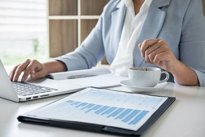 Midsection of woman working in office with documents and coffee cup on table