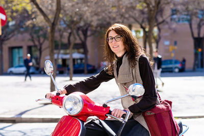 Happy cheerful girl driving scooter through city street.