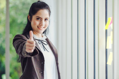 Portrait of a smiling young woman standing against wall