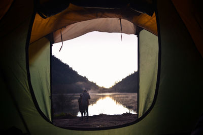 Friends standing by lake seen through tent