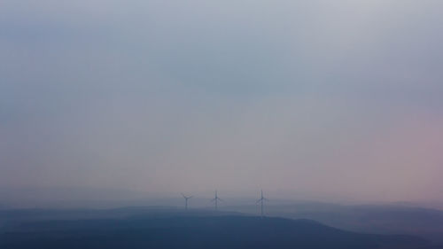 Silhouette of wind turbines on landscape against sky