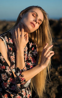 Beautiful young woman with eyes closed touching neck while standing on land