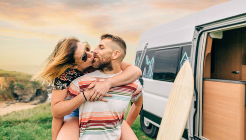 Couple kissing piggybacking next to their camper van during a trip