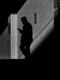 Silhouette man using phone while walking against building