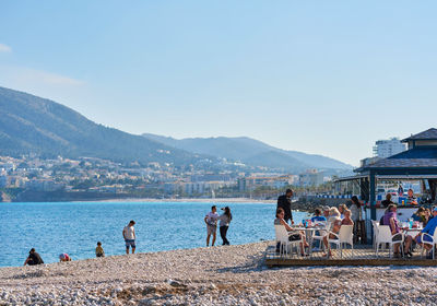 People on lake by mountains against clear blue sky