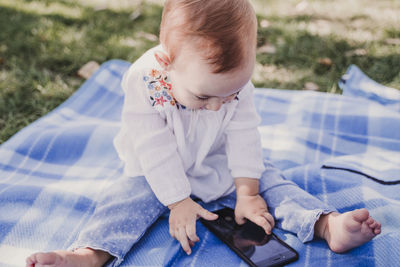 Close-up of cute baby girl using phone while sitting on picnic blanket