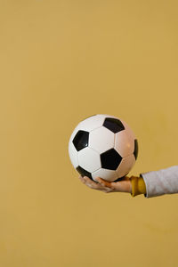 Close-up of hand holding ball against yellow background