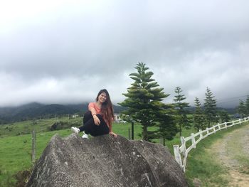 Portrait of young woman on rock against sky