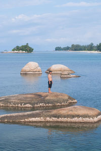 Shirtless man standing on rock amidst sea against sky