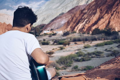 Rear view of man playing guitar on mountain