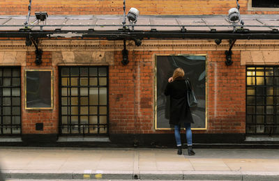 Full length rear view of woman standing against blank billboard on brick wall