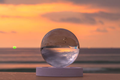 Close-up of crystal ball on water against orange sky