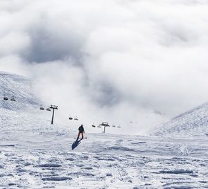 Rear view of snowboarder on snowcapped mountain against cloudy sky