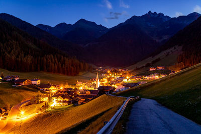 Road leading towards illuminated town against mountains