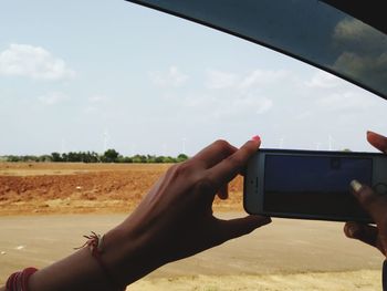 Midsection of person using mobile phone against sky