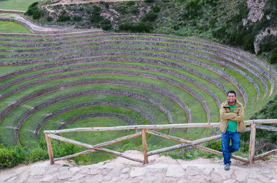 Full length portrait of smiling young man with arms outstretched standing against amphitheater