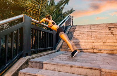 Young blonde woman doing doing push ups over railing banister at sunset