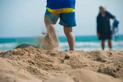 Low section of people on beach against sky