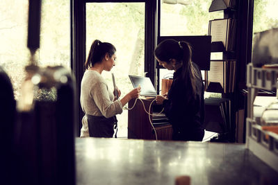 Female owner and colleague installing laptop for orders in cafe