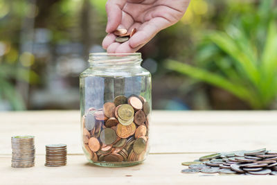 Cropped hand of man putting coins in jar on wooden table