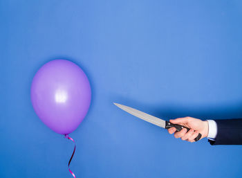Cropped hand of woman holding knife by balloon on table
