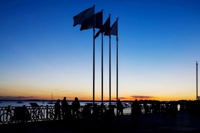 Silhouette people and flags by sea during sunset