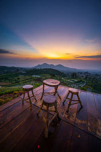 Empty chairs and tables against sky during sunset