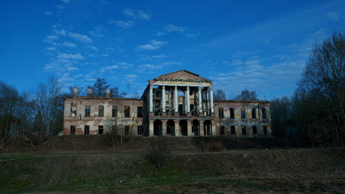 Old building by trees against blue sky