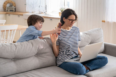 Freelancer mom working on laptop at home during lockdown, noisy child distracts asking attention.