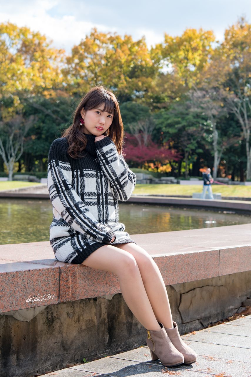 real people, tree, outdoors, one person, full length, park - man made space, day, sitting, casual clothing, front view, leisure activity, lifestyles, focus on foreground, young women, sunlight, young adult, looking at camera, childhood, nature, retaining wall, beautiful woman, sky, people