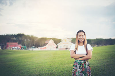 Portrait of smiling woman with arms crossed standing on field