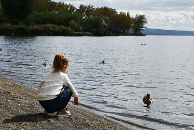 Rear view of girl crouching at lakeshore