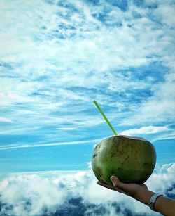 Close-up of hand holding apple against blue sky