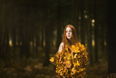 Portrait of woman standing by tree in forest