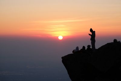 Silhouette hikers standing on cliff against sky during sunset