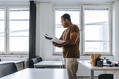 Focused male professor reading test papers while standing in classroom at junior high school