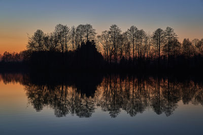 Silhouette trees by lake against sky during sunset