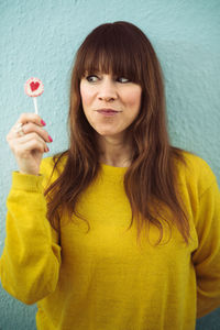 Woman having lollipop while standing against wall