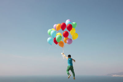 Girl holding balloons flying against sky