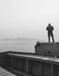 Rear view of man standing by railing against sky