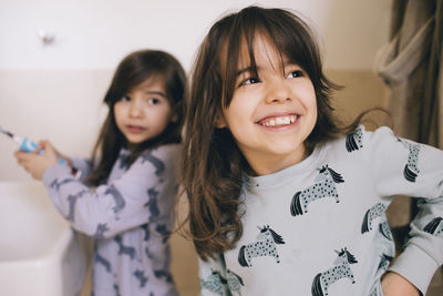 Happy girl standing with sister holding toothbrush in bathroom