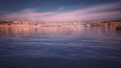 Illuminated buildings by sea against sky during sunset
