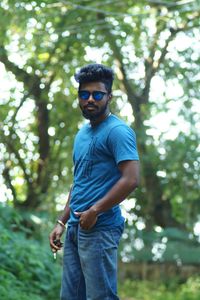 Portrait of young man standing against trees in forest