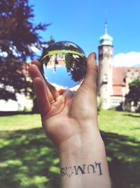 Midsection of person holding glassball against trees and castle