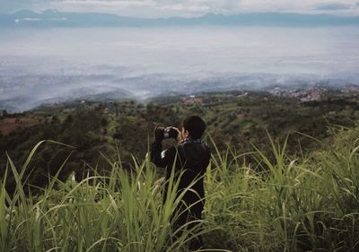 Rear view of man photographing landscape by plants