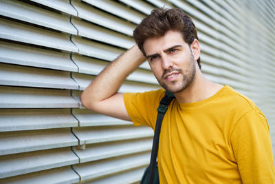 Portrait of young man standing by wall outdoors