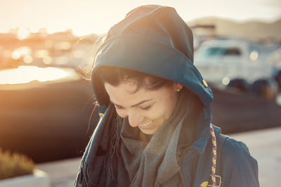 Young woman with rain coat in ibiza city port at sunset, smiling and looking down