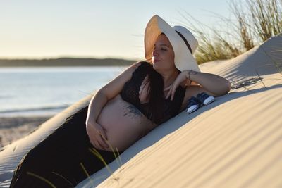 Young woman sitting on beach against sky